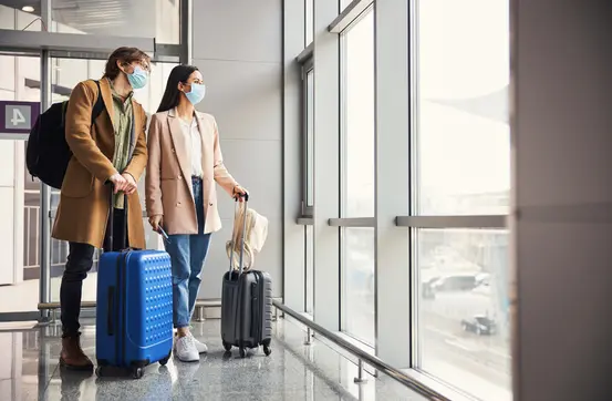 A couple in face masks standing at the airport, preparing for their journey with luggage, showcasing the start of their travel process after visa application and flight booking.