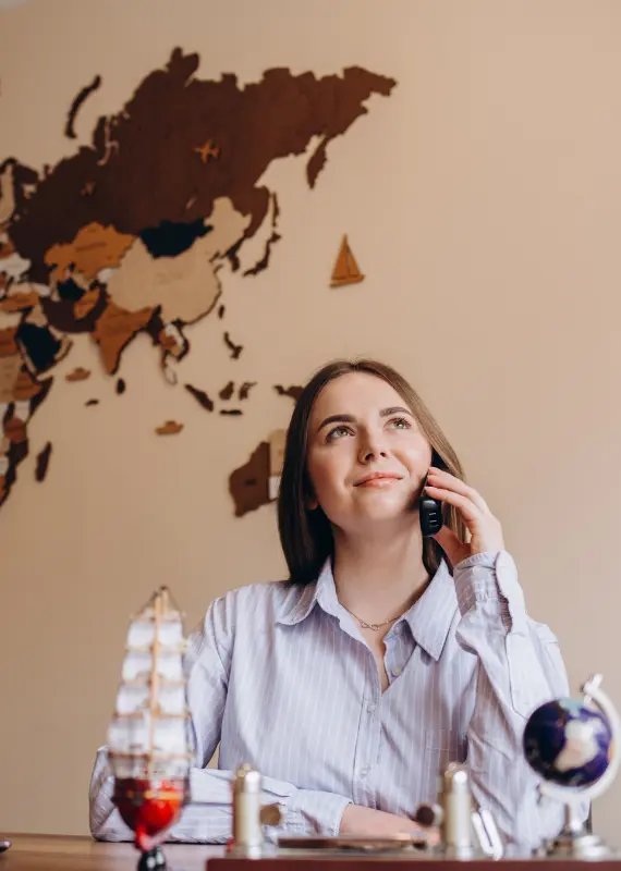 A woman talking on the phone, assisting with travel services like visa applications and flight bookings, with a world map in the background.